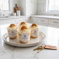 Four cups of layered pudding on a ceramic serving tray beside house keys on a white marble counter in a staged kitchen.