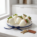 Six white-chocolate-dipped strawberries on a ceramic plate beside a brass welcome-home keychain on a white marble counter.